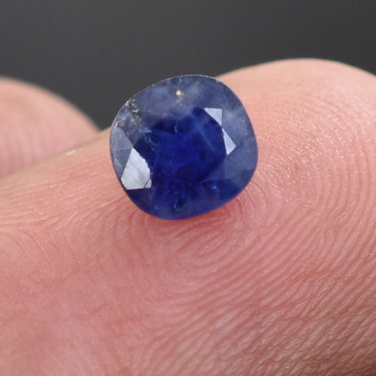 Deep blue faceted sapphire gemstone resting on a fingertip.