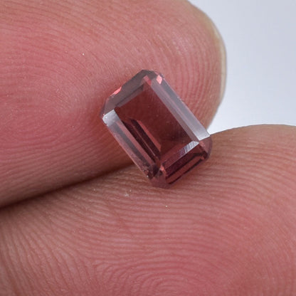 Faceted red gemstone held between two fingertips.