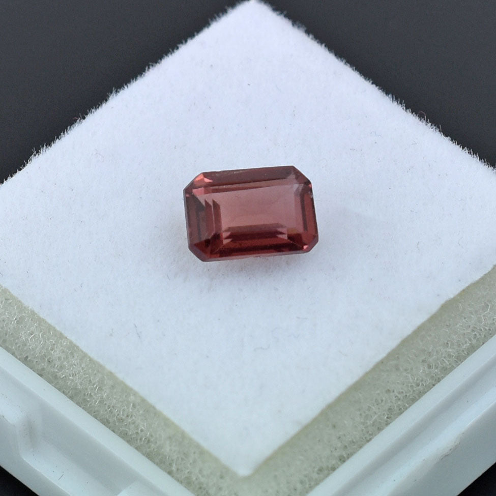 Rectangular-cut pink gemstone with a reddish hue.