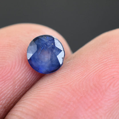 Blue faceted gemstone, likely a sapphire, resting on a fingertip.