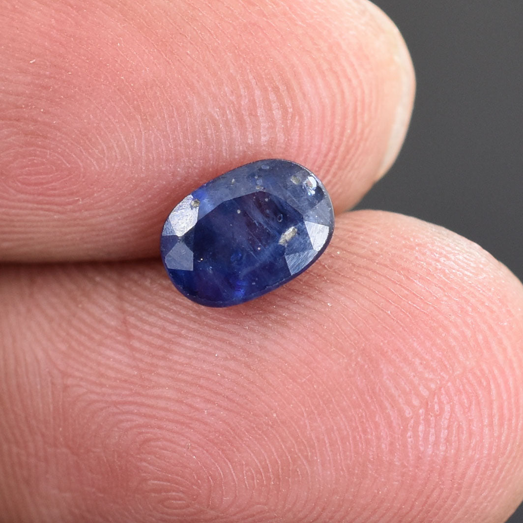 Oval-cut blue sapphire gemstone held between two fingers.