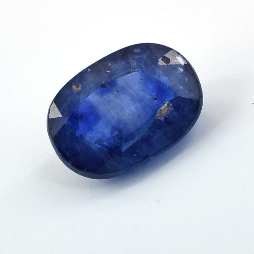 Oval-cut deep blue gemstone with facets and inclusions.