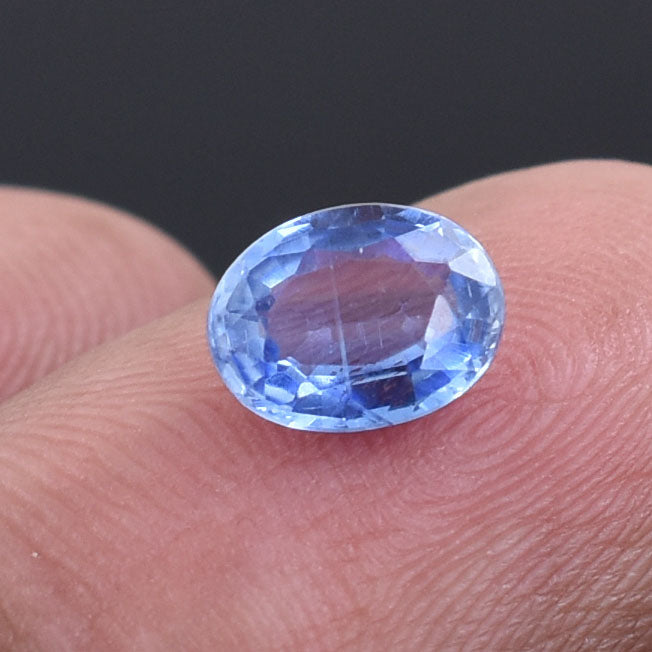 Oval-cut blue gemstone, likely a sapphire, resting on a fingertip.