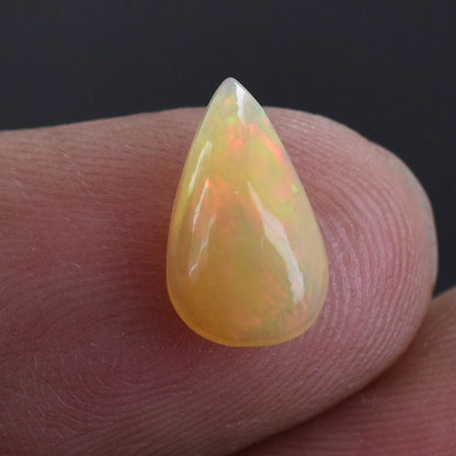 Teardrop-shaped opal gemstone with a yellow-orange hue and iridescent flashes.