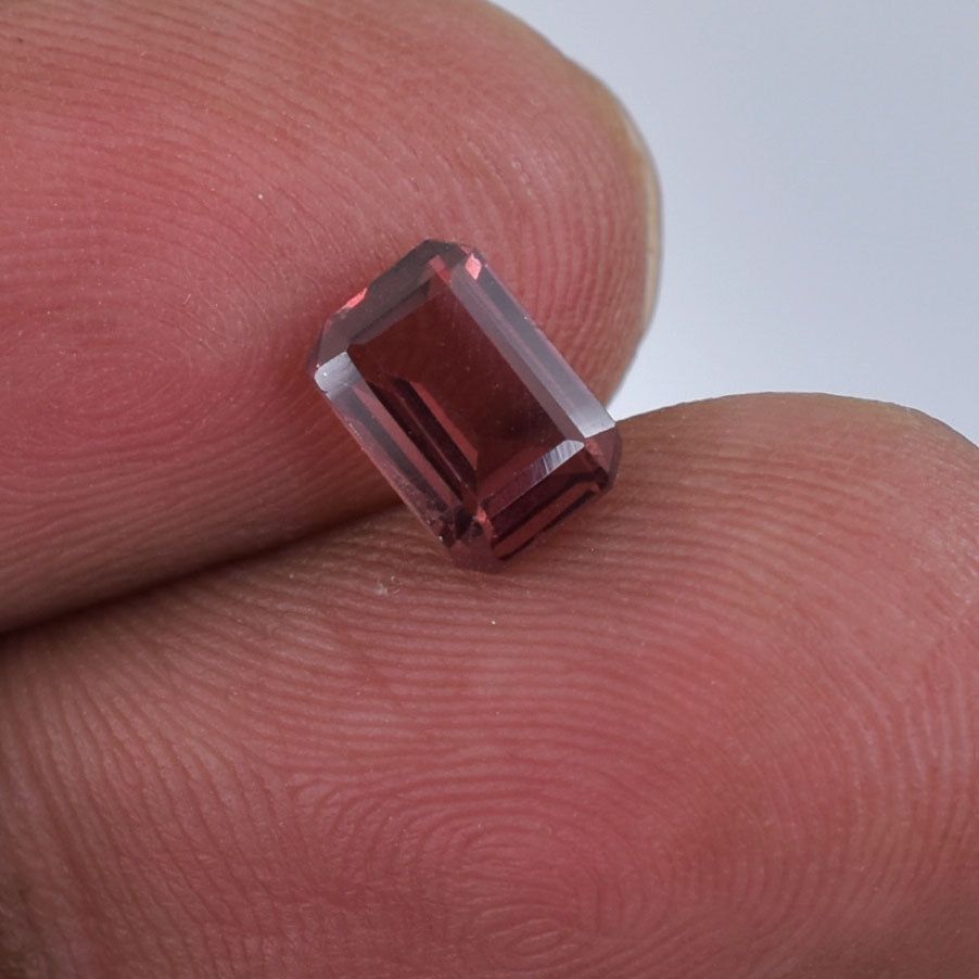 Rectangular-cut red gemstone held between two fingertips.