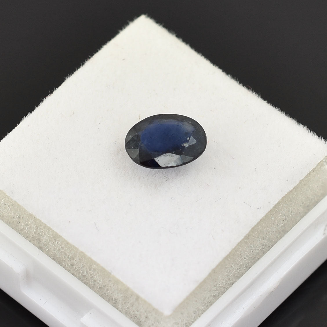 Oval-shaped blue sapphire gemstone on a white display pad.