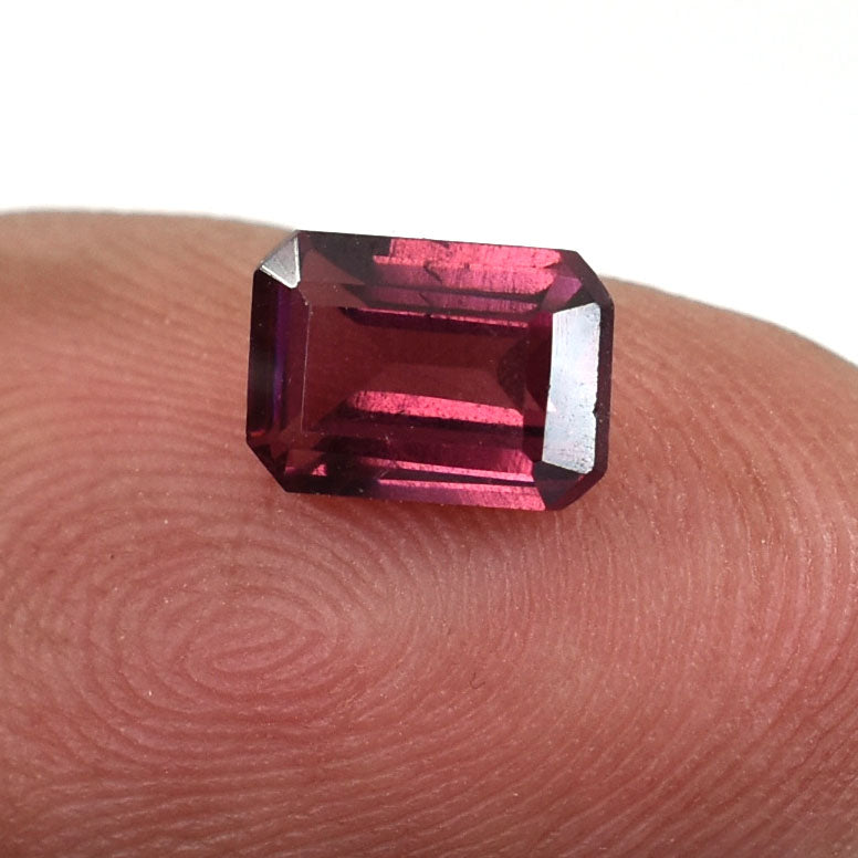 Deep red, emerald-cut gemstone resting on a fingertip.