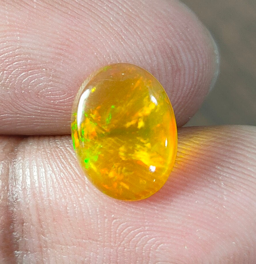 Oval-shaped opal gemstone with vibrant yellow-orange color and green flashes.