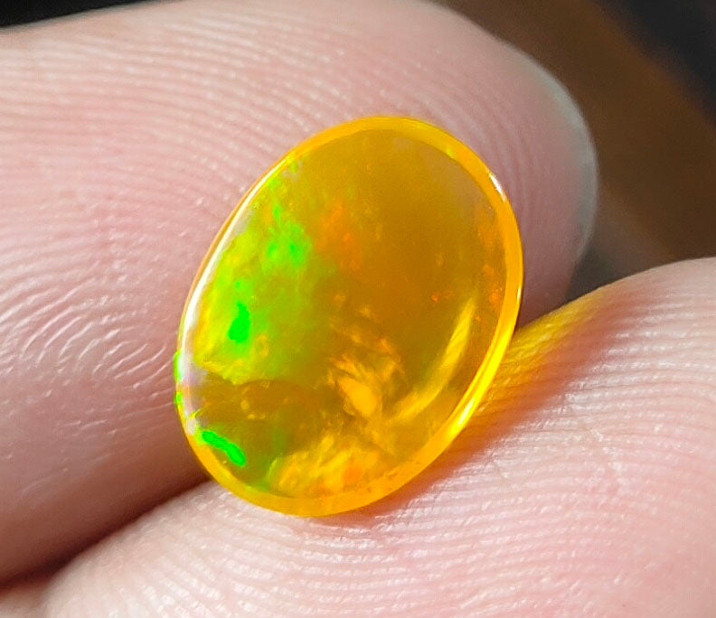 Vibrant yellow and green opal gemstone held between fingers.