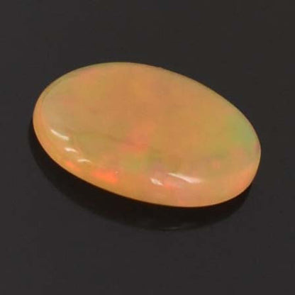 Oval-shaped opal gemstone with a milky yellow-orange color and subtle flashes of green and red.