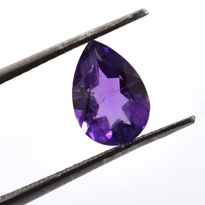 Pear-shaped purple gemstone held between tweezers.