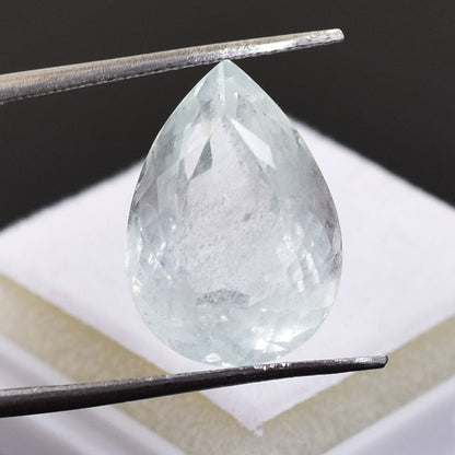 Teardrop-shaped, transparent gemstone held by tweezers.