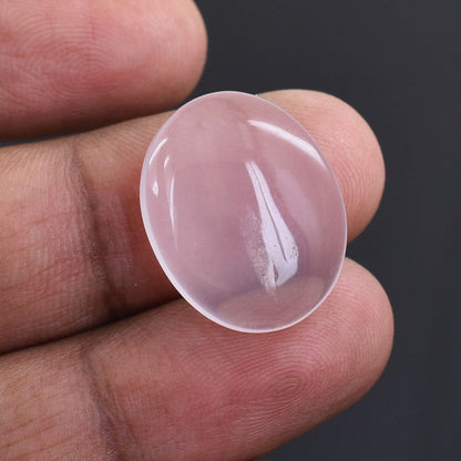 Oval-shaped, translucent pink gemstone or crystal held between fingers.