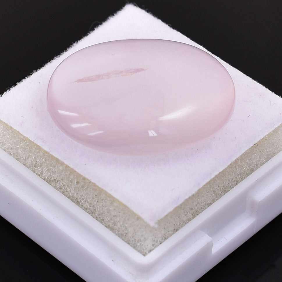 Smooth, oval-shaped pink gemstone or crystal on a white surface.