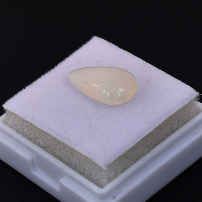 Teardrop-shaped white or cream-colored gemstone or cabochon on a light-colored display pad.