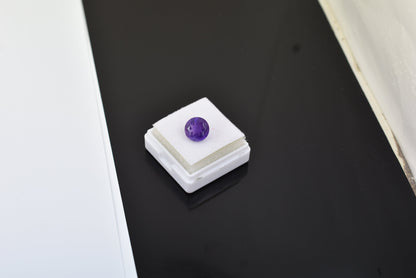 Purple gemstone or bead sitting on a small white display stand.