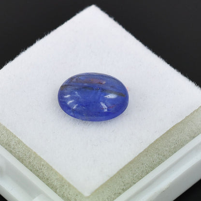 Oval-shaped blue gemstone or sapphire on a white surface.