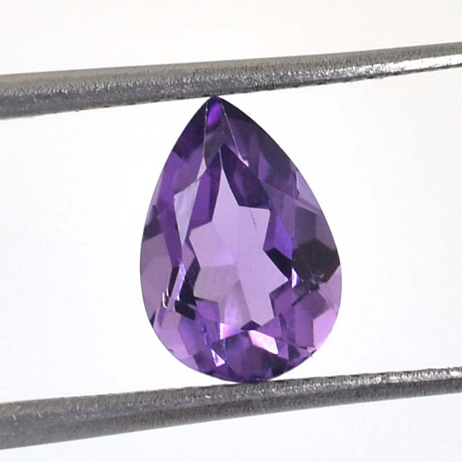 Pear-shaped purple gemstone, likely an amethyst, held by tweezers.