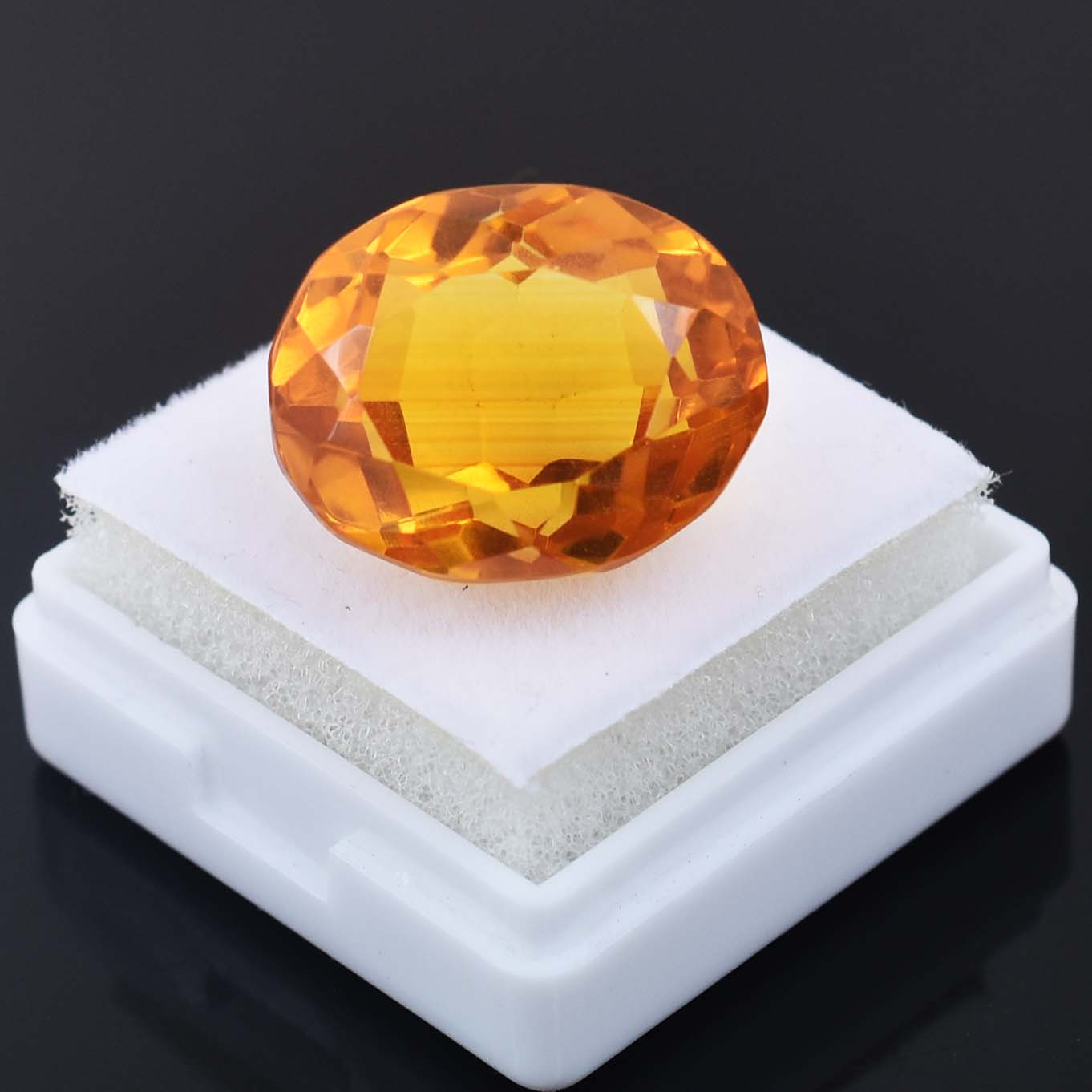 Faceted oval-shaped orange gemstone on a white display stand.