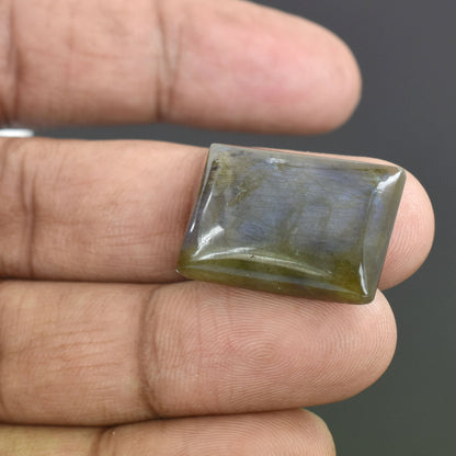 Rectangular gemstone with a greenish-yellow hue held between fingers.