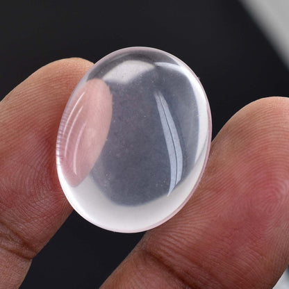 Clear, oval-shaped glass or crystal cabochon held between two fingers.