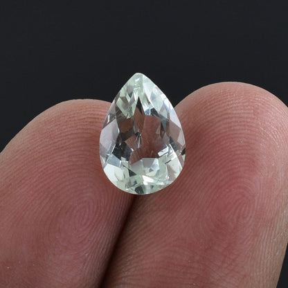 Pear-shaped, faceted clear gemstone held between fingertips.