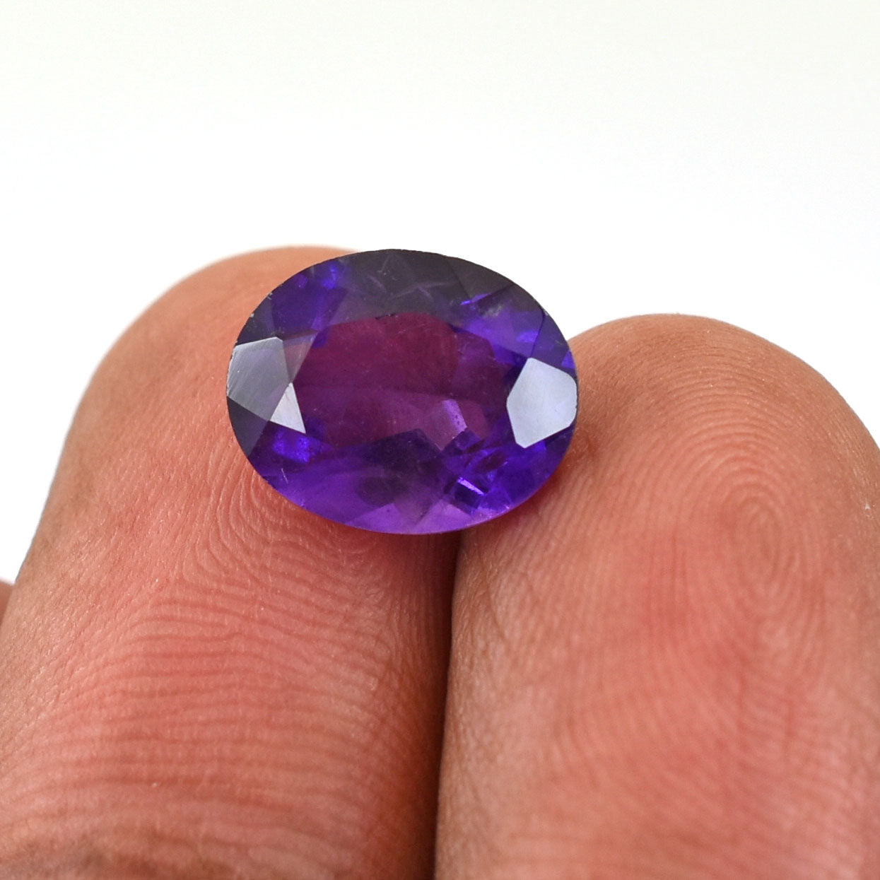 Deep purple oval-cut gemstone, likely an amethyst, held between fingers.