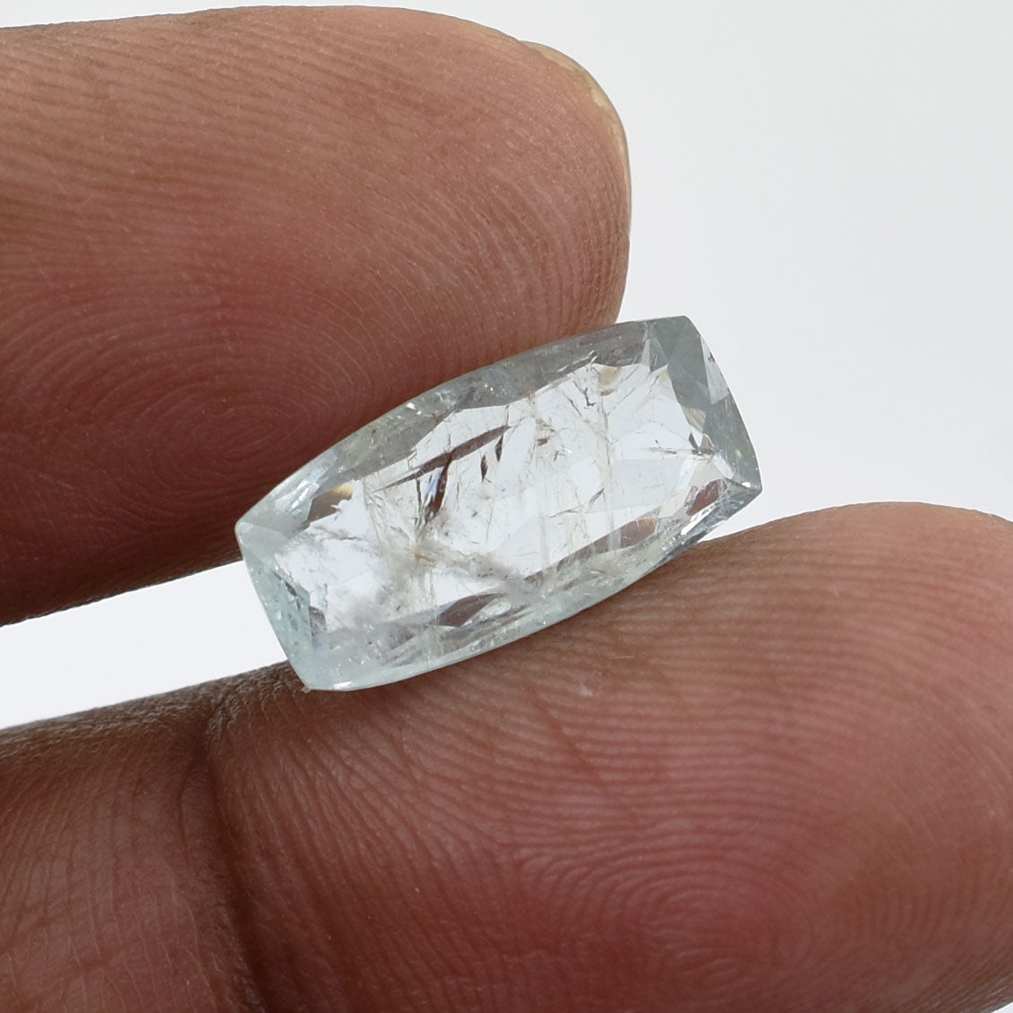 Raw, uncut aquamarine gemstone held between two fingers.