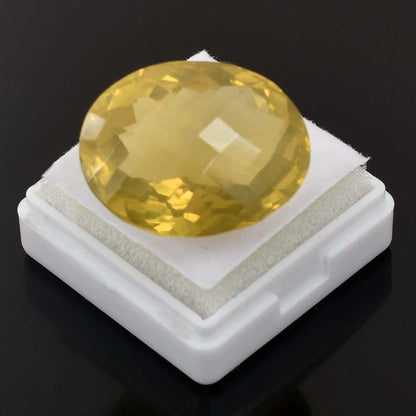 Faceted yellow gemstone or crystal sitting on a white display stand.