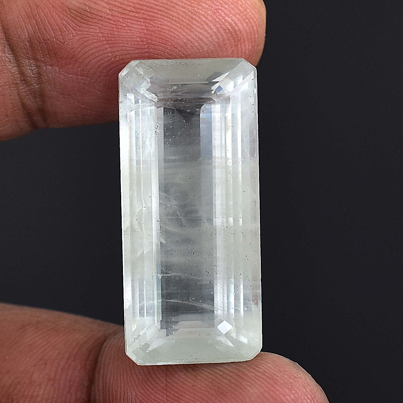 Clear, rectangular-cut gemstone or crystal held between fingers.