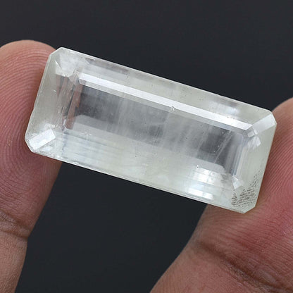 Clear, rectangular gemstone or crystal held between two fingers.