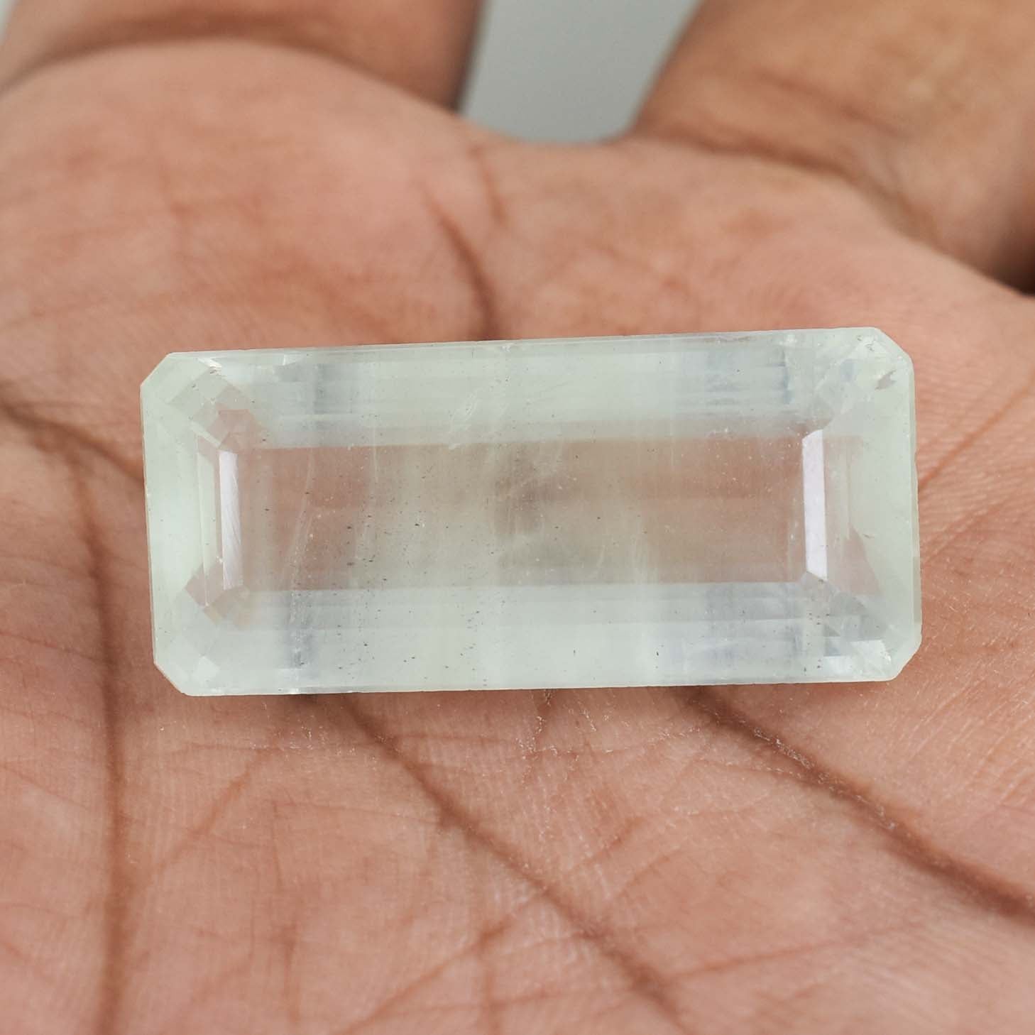 Rectangular, transparent gemstone or crystal held in a person’s palm.