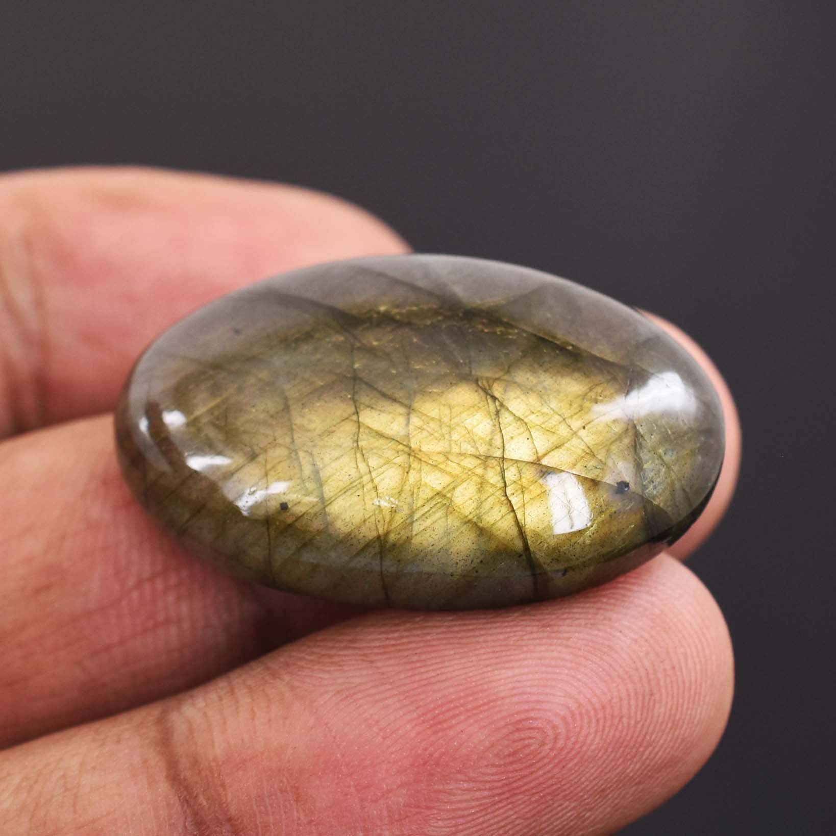 Smooth, oval-shaped gemstone with golden-green internal inclusions held between fingertips.