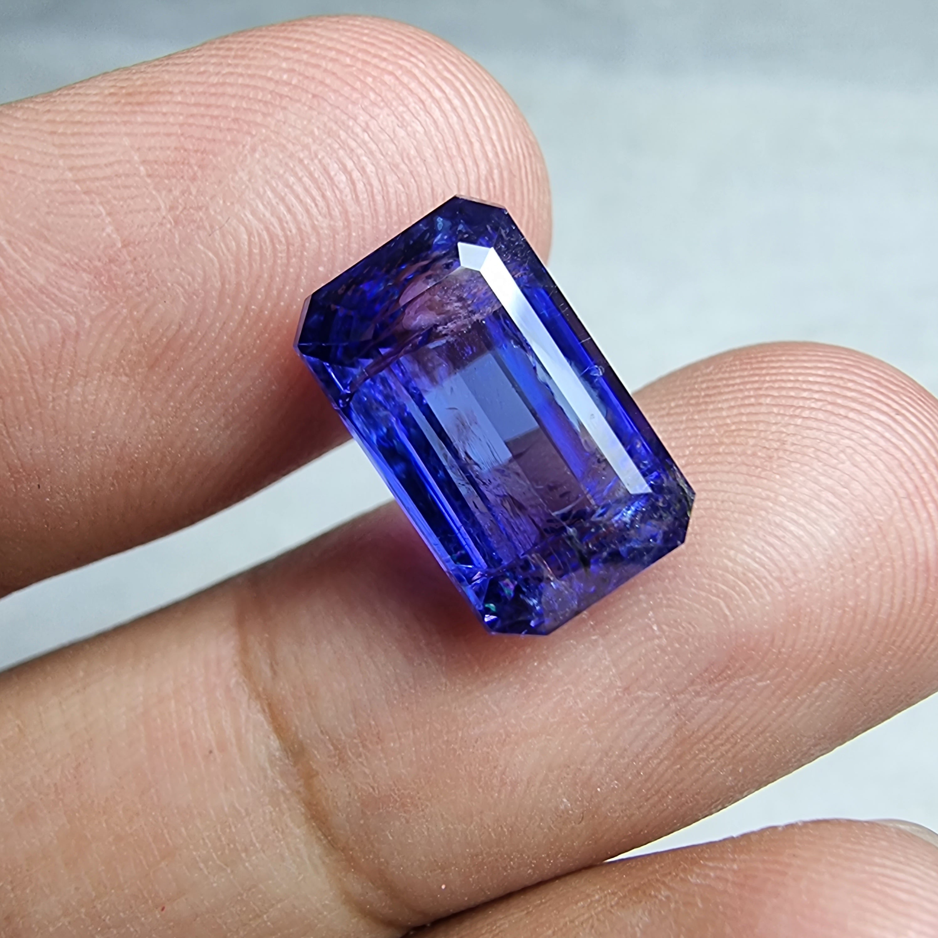 Vibrant blue emerald-cut gemstone held between two fingers.