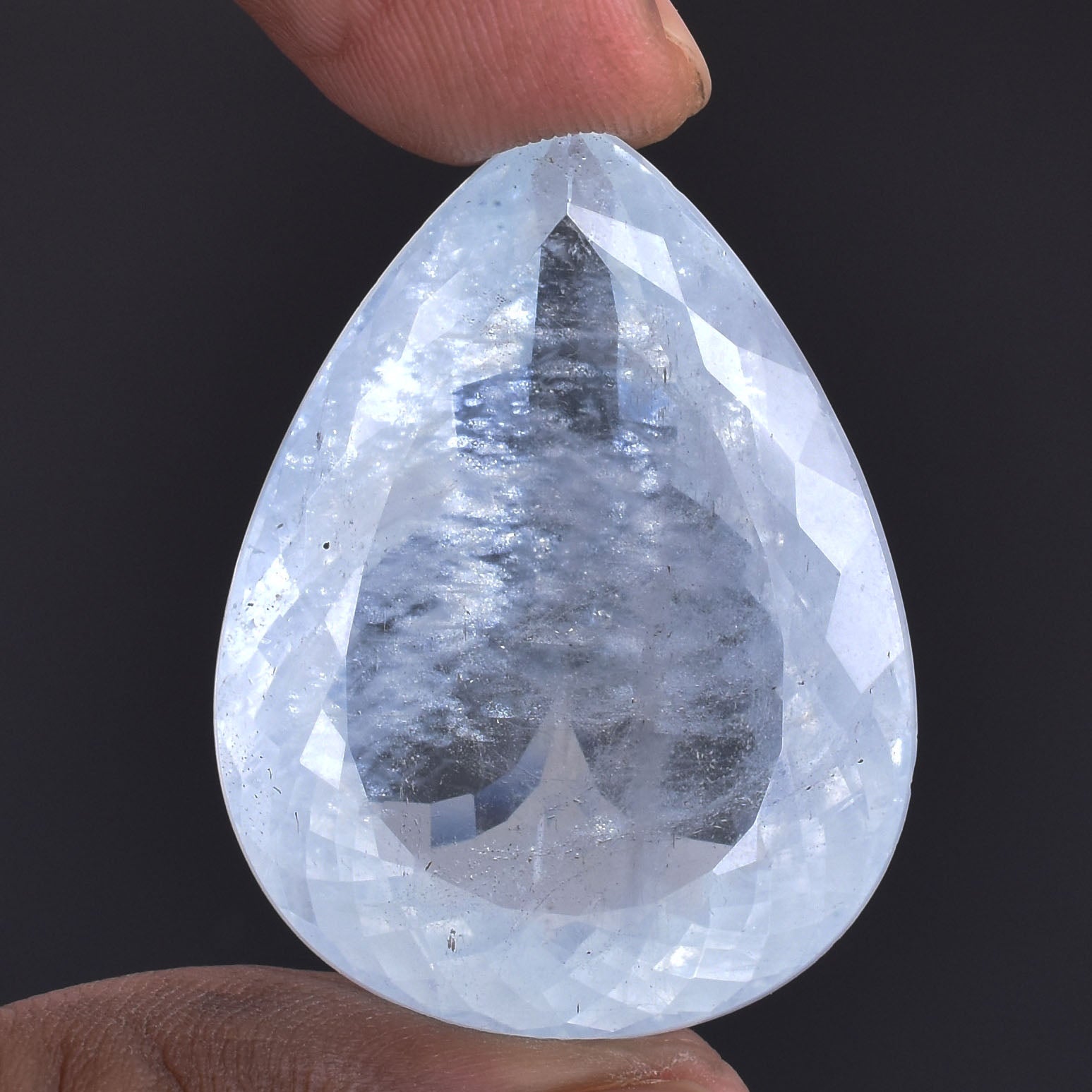 Teardrop-shaped, translucent gemstone or crystal held between fingers.