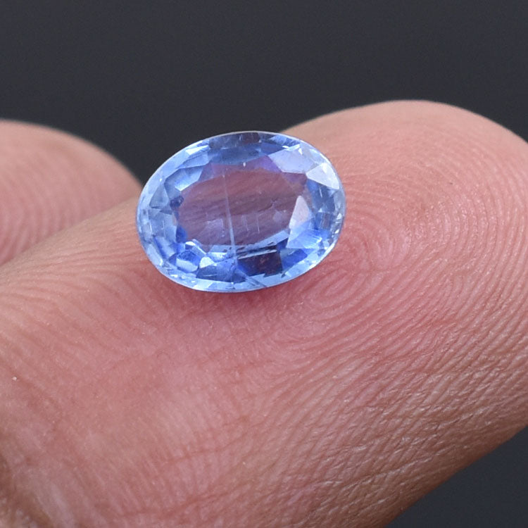 Oval-cut blue gemstone, likely a sapphire, resting on a fingertip.