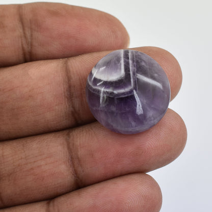 Spherical purple gemstone or crystal with white streaks held between fingers.