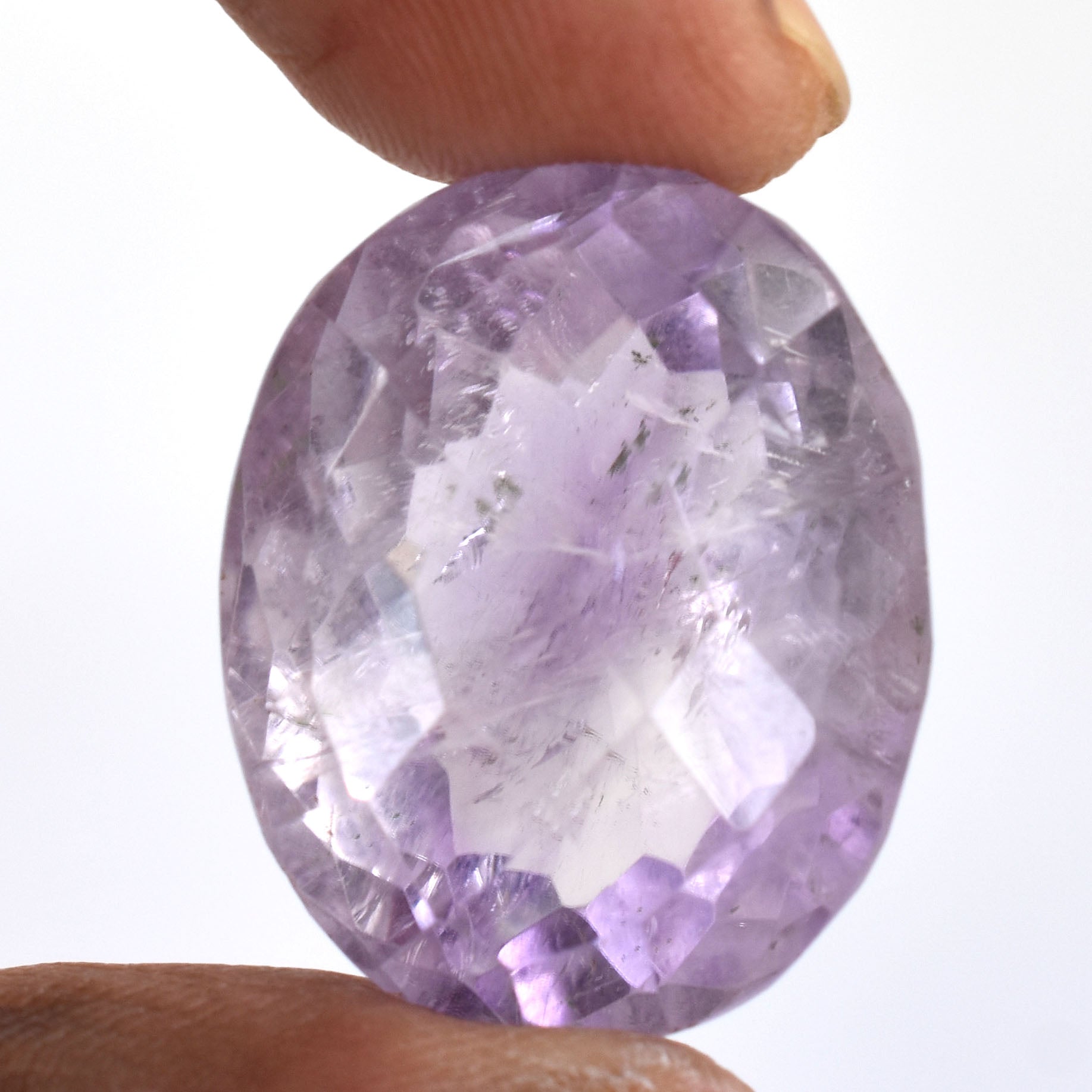 Oval-cut light purple gemstone, likely an amethyst, held between fingers.