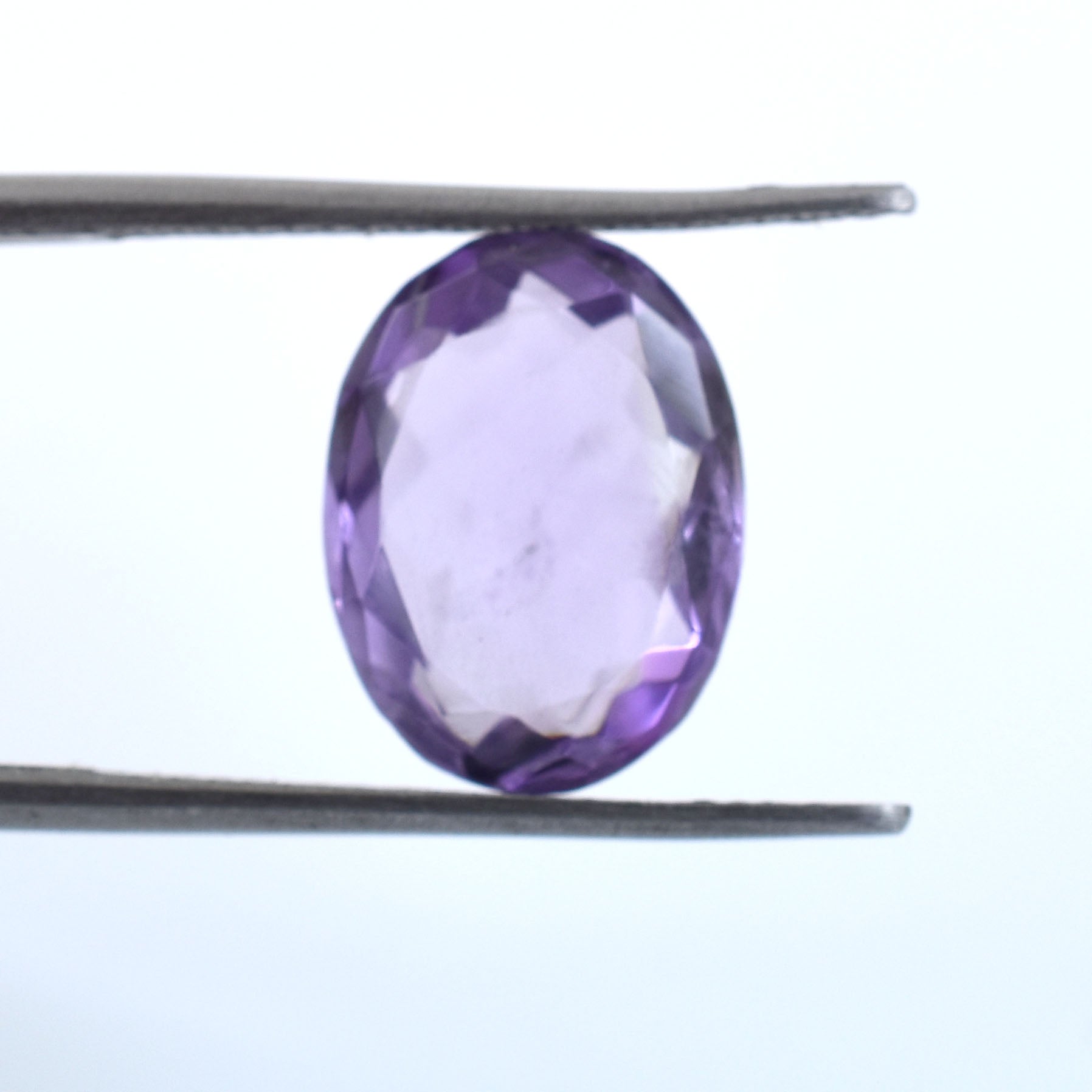 Oval-cut purple gemstone held between tweezers.