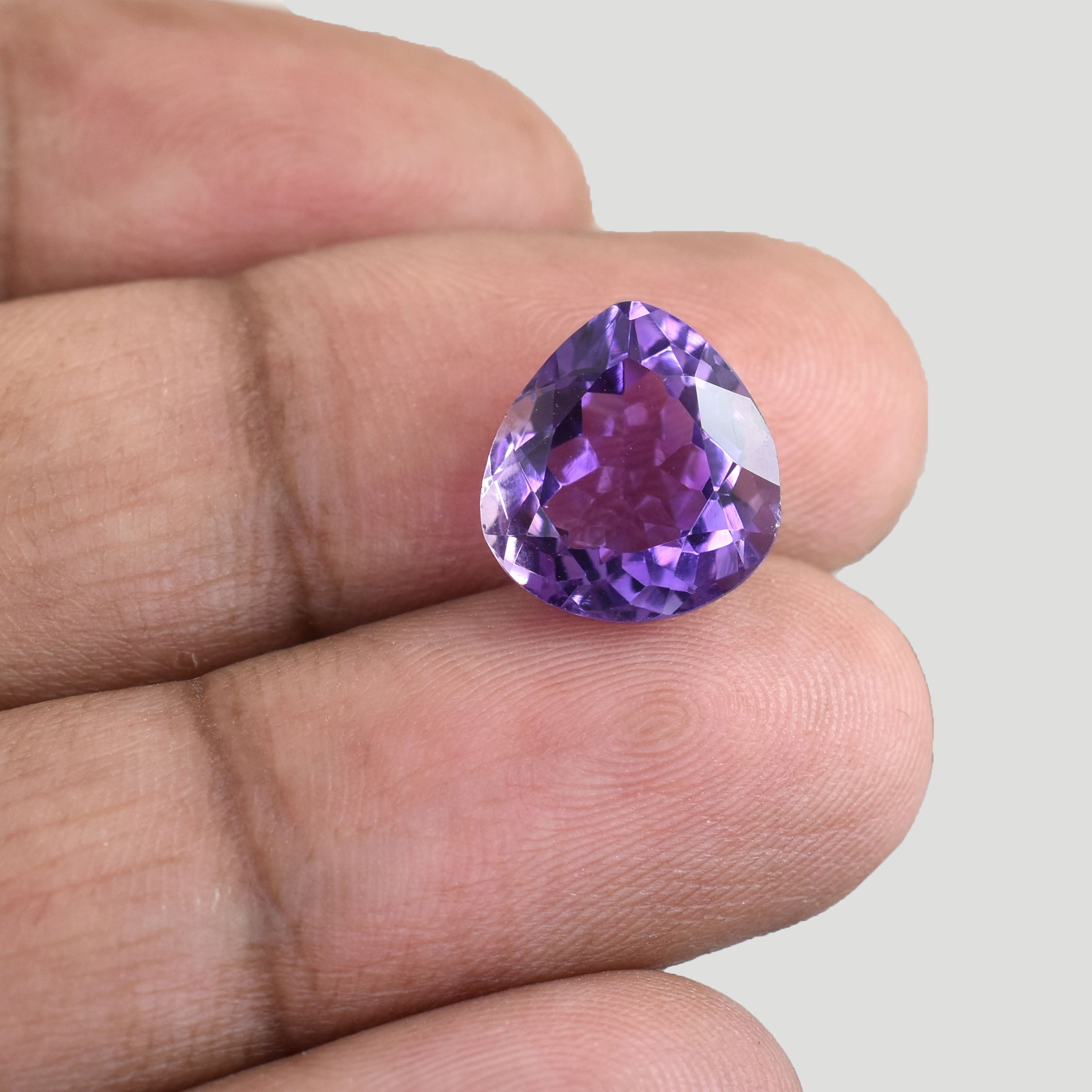 Heart-shaped purple gemstone held between fingers.