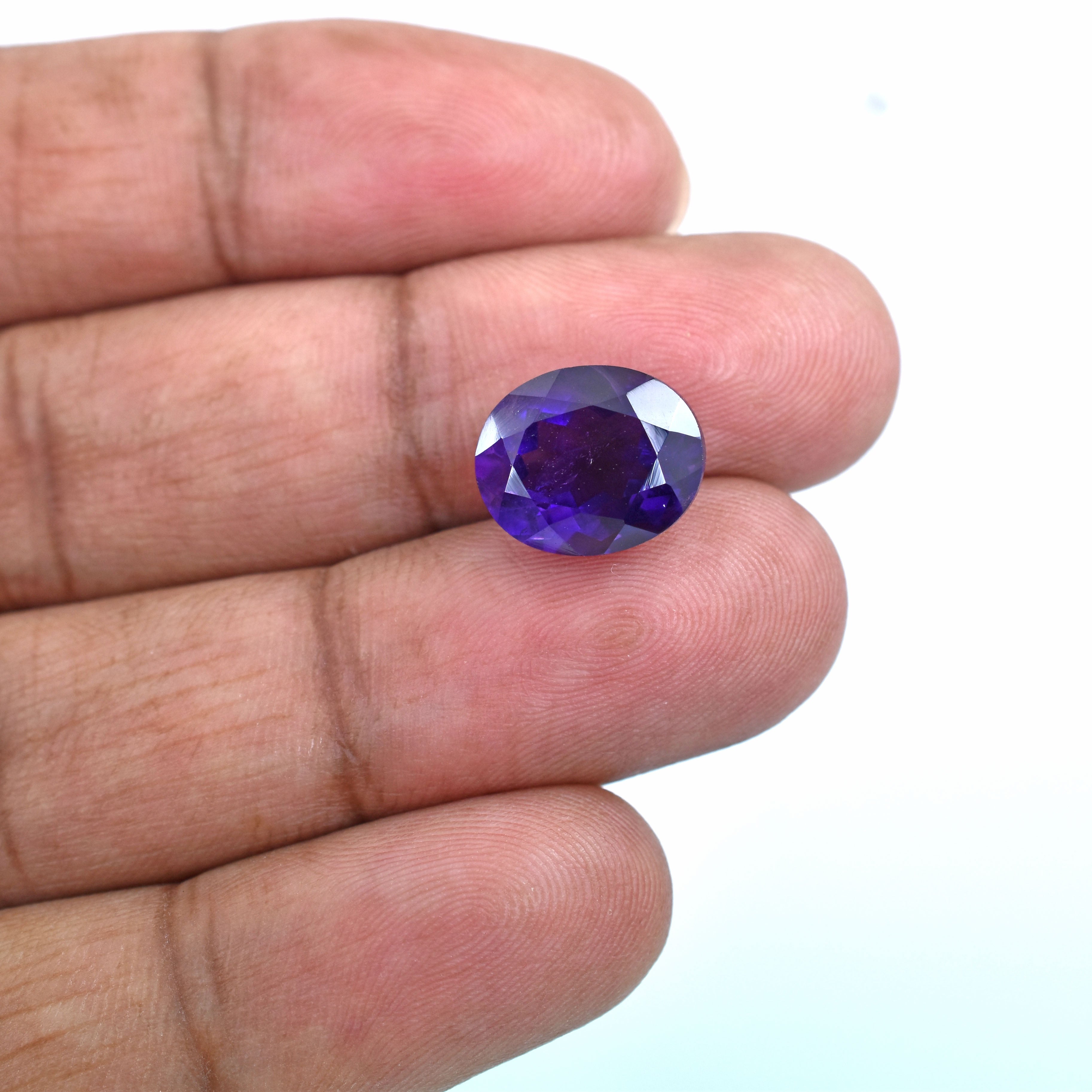 Oval-cut purple gemstone held between fingers.