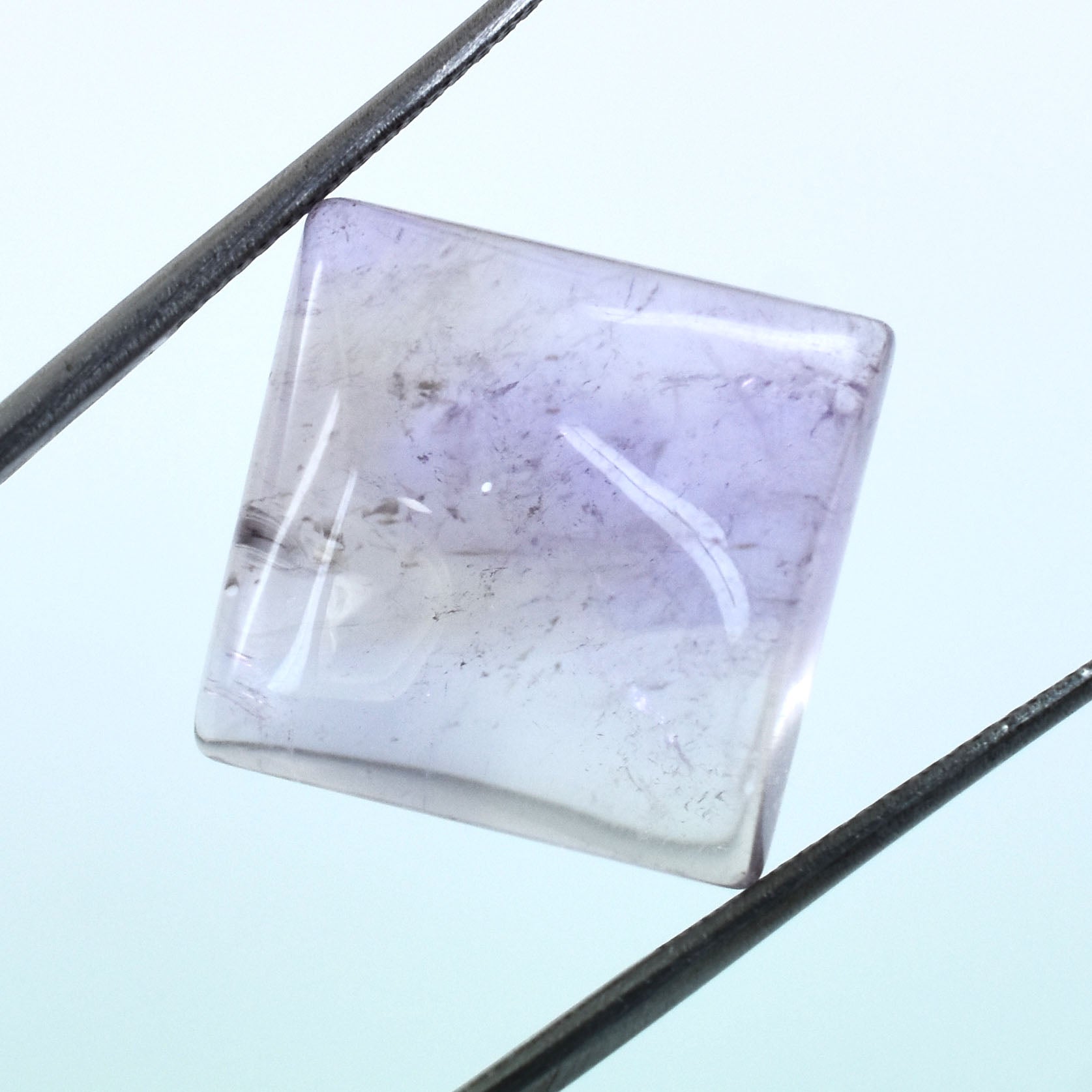 Square-cut gemstone with a pale lavender color and internal inclusions.