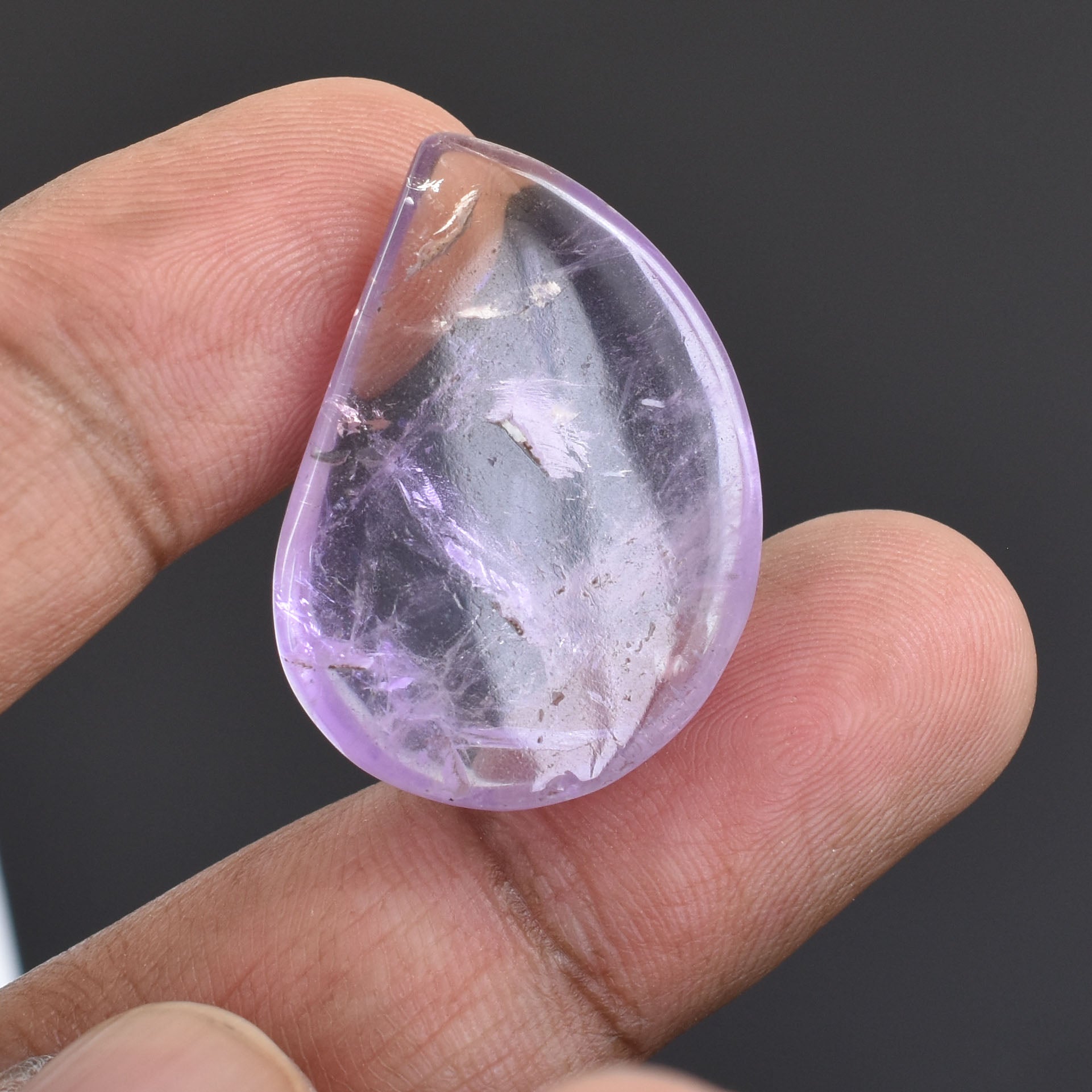 Teardrop-shaped amethyst crystal held between two fingers.