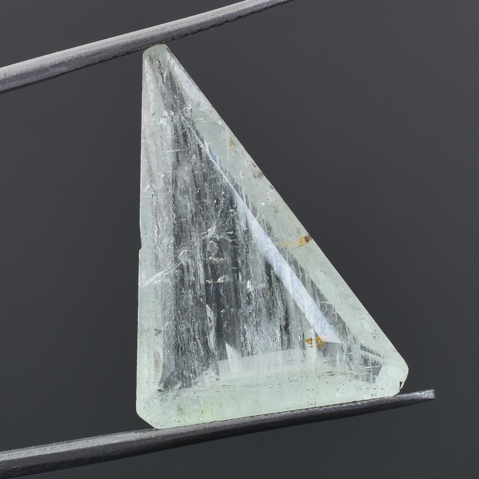 Triangular crystal or gemstone held by tweezers or forceps.