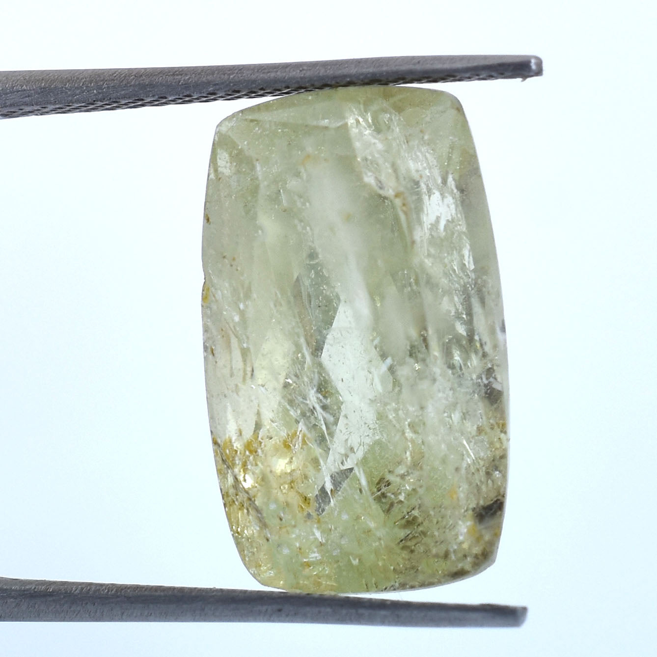 Pale green, semi-transparent gemstone or crystal held by tweezers.