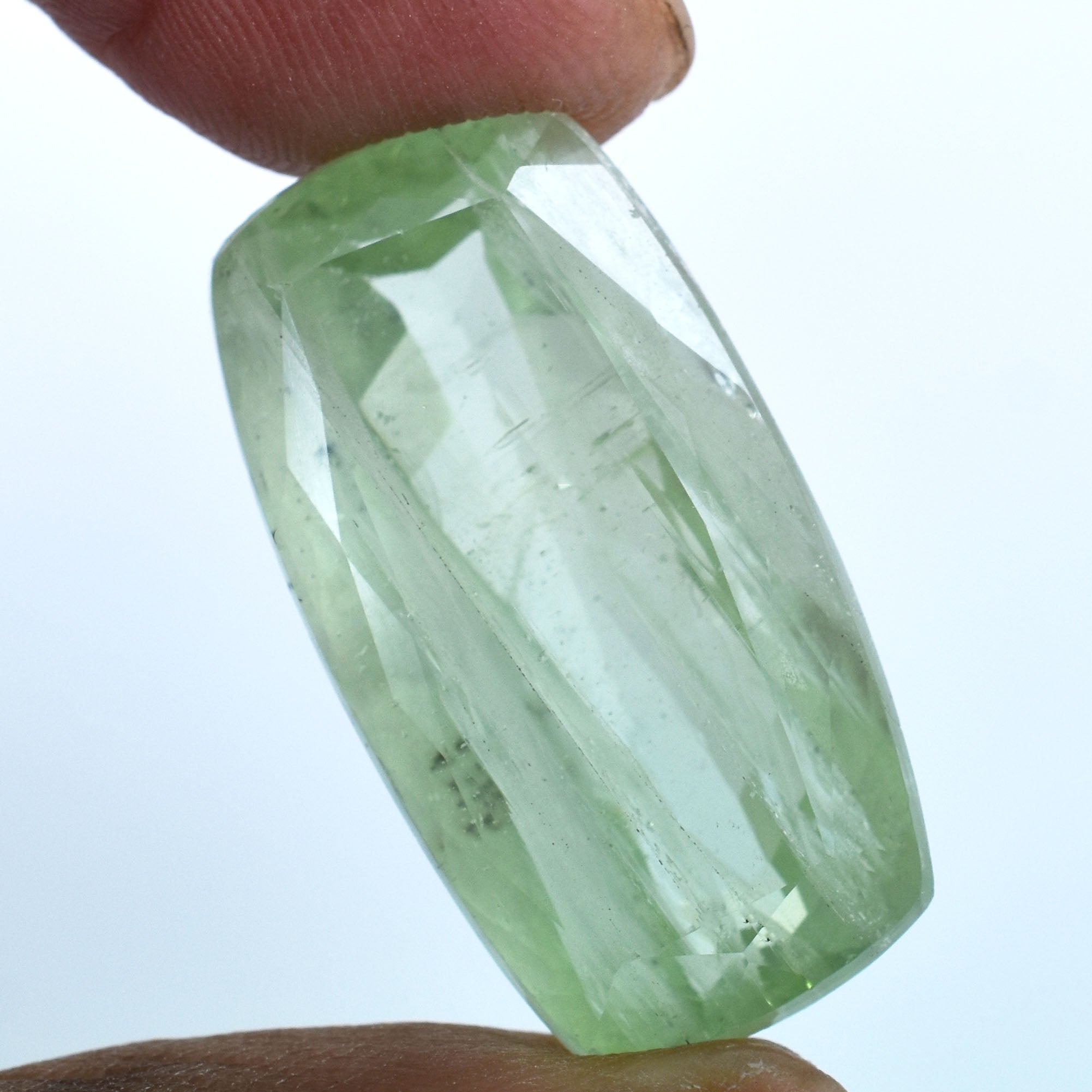 Pale green, faceted gemstone held between two fingers.