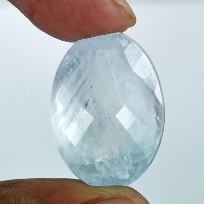 Faceted, pale blue gemstone or crystal held between two fingers.