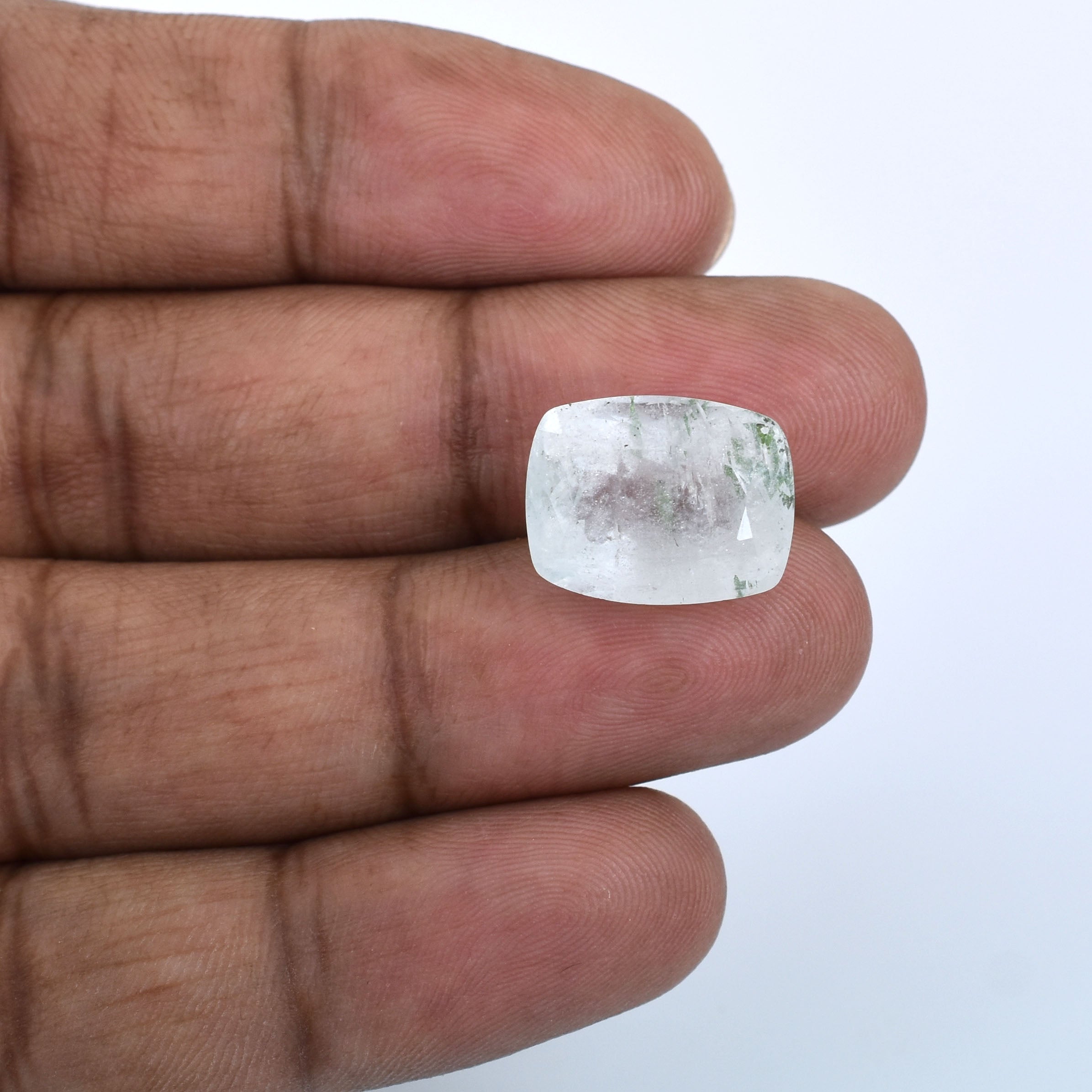 Rectangular cut, pale blue gemstone held between fingers.