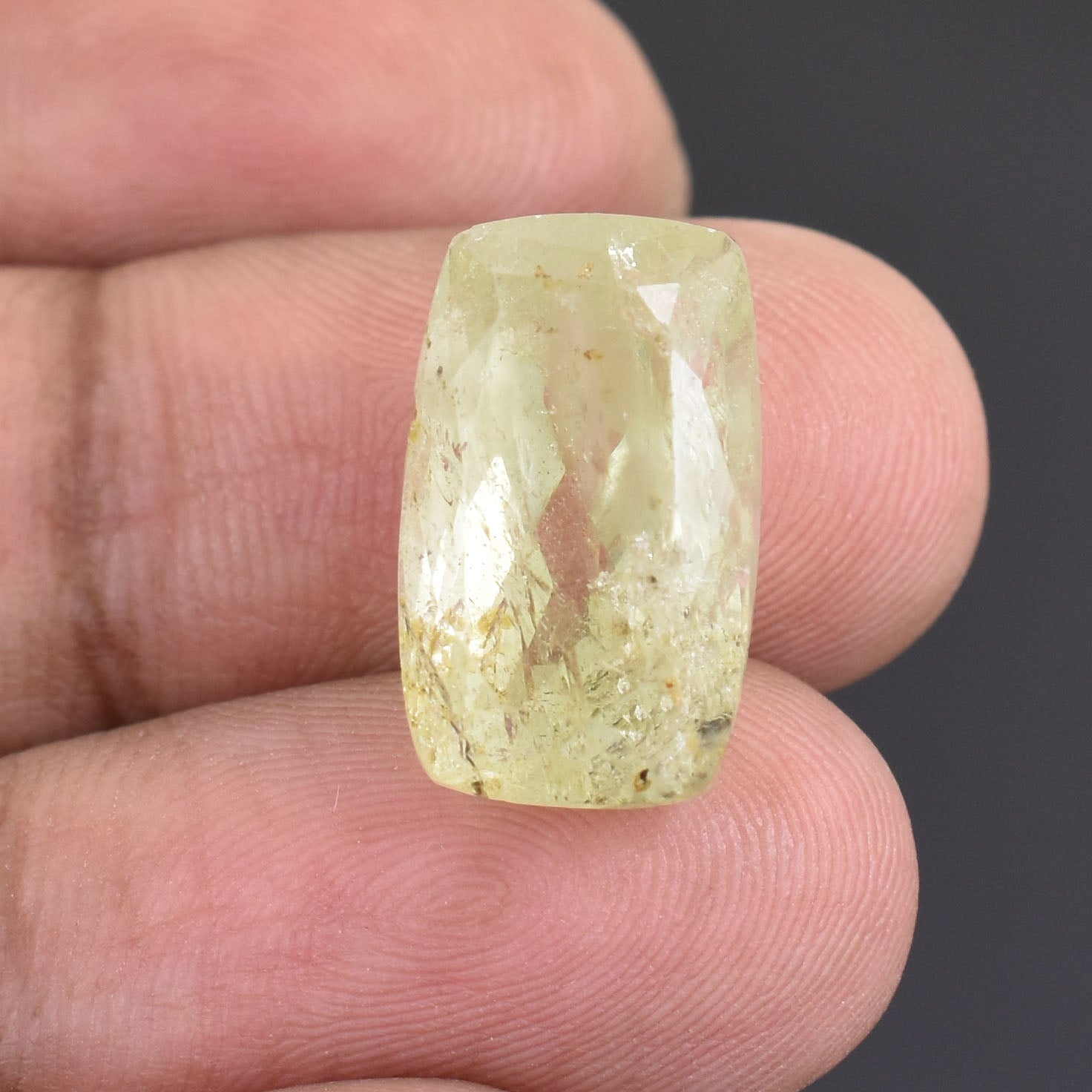 Pale yellow, rectangular gemstone held between fingertips.