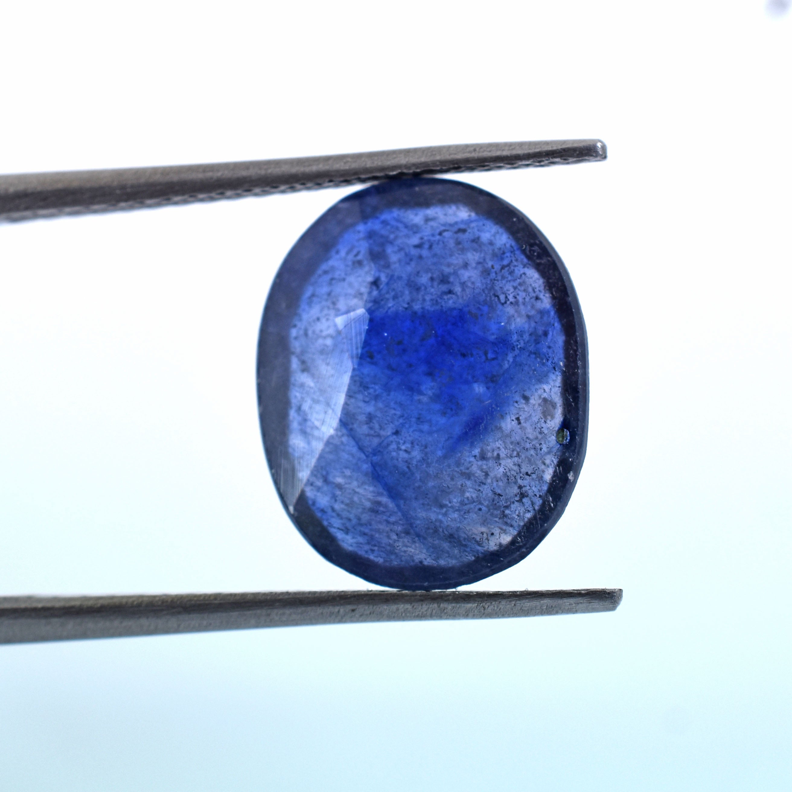 Oval-shaped blue gemstone held between tweezers.